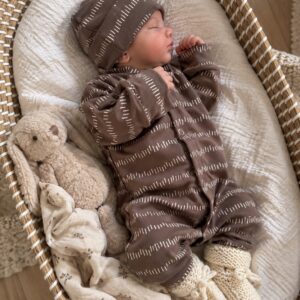 Slapende baby in een rieten wieg, gekleed in een bruin pakje en mutsje, naast een knuffelkonijn